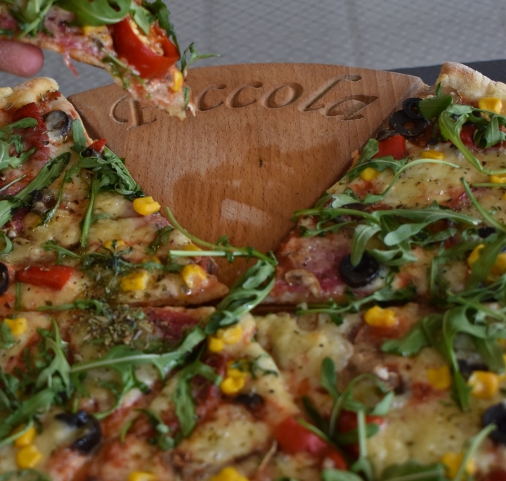 Kawałek pizzy z rukolą podawany w Pizzerii Piccola